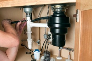 Plumber repairing a garbage disposal beneath a kitchen sink in Holly Springs