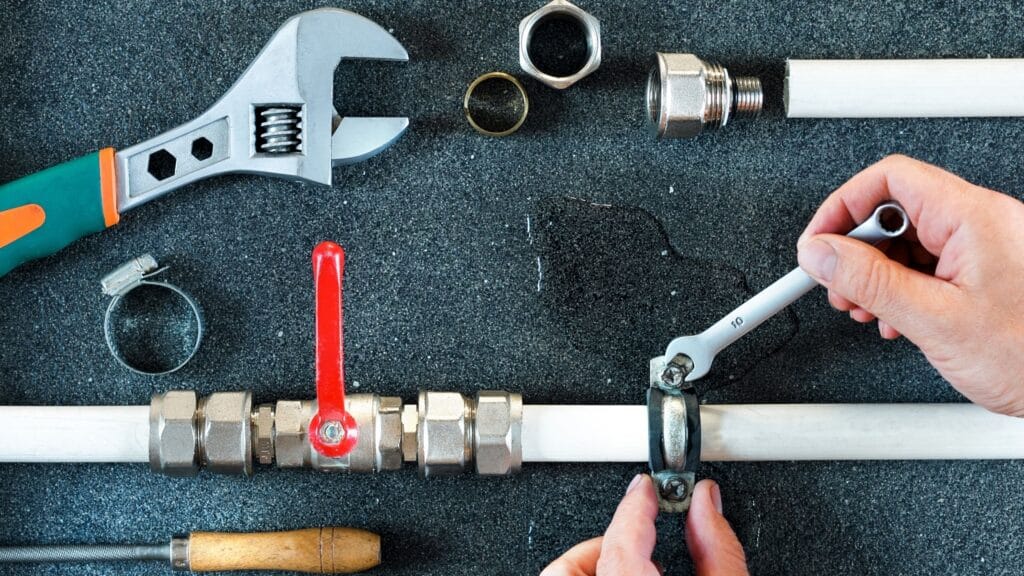 Plumber repairing a pipe valve with an adjustable wrench in Holly Springs