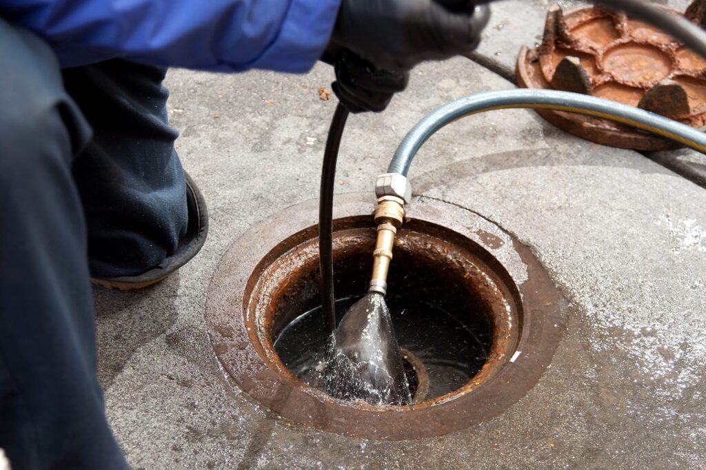 Plumber hydro jetting a sewer line through a manhole in Holly Springs