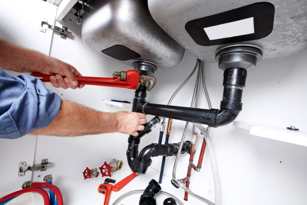 Plumber repairing drain pipes beneath a kitchen sink in Holly Springs